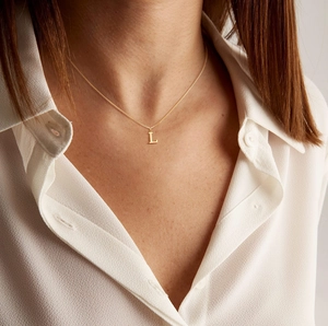 Detail of a minimalist gold necklace featuring a polished letter L pendant on a fine chain