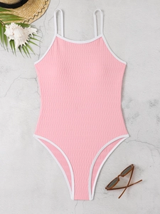 Flat lay of pink one-piece swimsuit with white trim and textured fabric on stone background