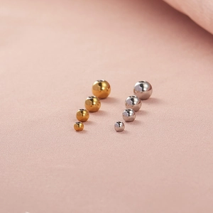 Various sizes of gold and silver stainless steel beads on a soft pink fabric background