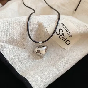 Minimalist silver heart pendant necklace with black wax rope on a linen texture