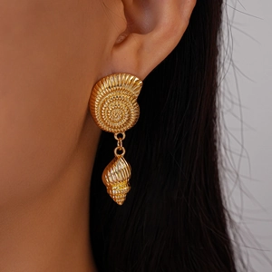 Close-up of a gold shell-shaped earring on a woman's ear with nautical nautilus details