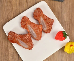 Macro detail of three realistic artificial lamb rib food models on a white ceramic plate