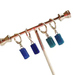 Golden hoop earrings with cylindrical blue natural stone pendants on a metal display stand
