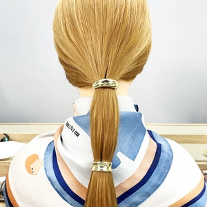 Detail of golden metal hair tie ponytail holder on blonde hair with smooth finish