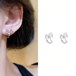 Detail of silver bow huggie earrings with intricate hollow design on ear and white background