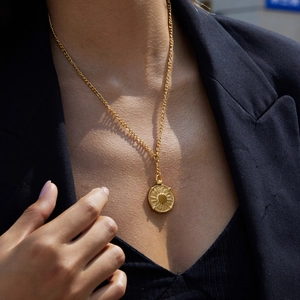 Close-up of a golden coin necklace with sunburst pendant worn by a model in a black suit