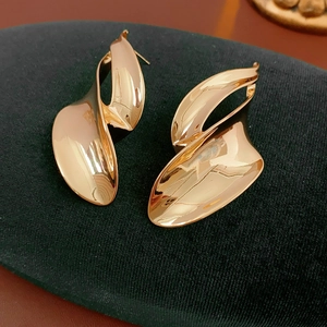 Macro shot of twisted golden leaf earrings on a green velvet surface showing detail