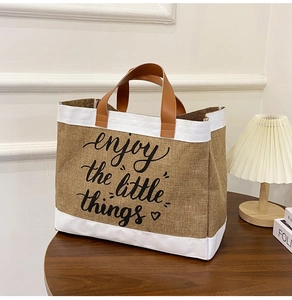 Dettaglio borsa in lino con manici in pelle marrone e scritta enjoy the little things
