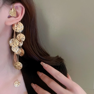 Dettaglio dell'orecchino a clip dorato con nappe lunghe e paillettes metalliche martellate