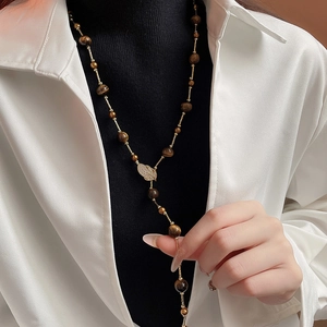 Long gold necklace featuring tiger eye beads and a leaf pendant on black clothing