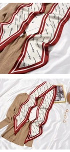 Detail of a vintage long silk scarf with red borders and script print on beige knitwear