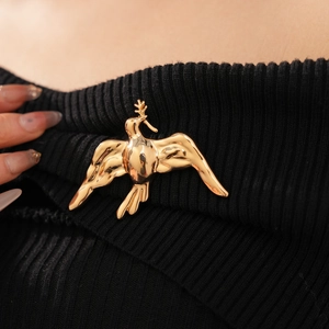 Detailed close-up of a golden bird brooch with olive branch on black knit fabric