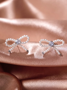 Macro shot of pearl bow earrings with a zircon center on elegant champagne silk fabric