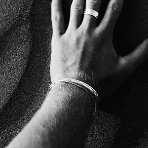 Artistic monochrome detail of stainless steel cuff and ring on hand over sand