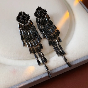 Detail shot of black rhombus zircon tassel earrings on a textured white surface
