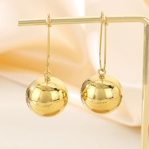 Detailed view of polished gold sphere drop earrings hanging on a metal stand