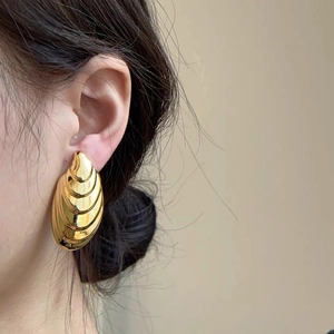 Close-up of model wearing textured gold shell-shaped earrings with wave patterns