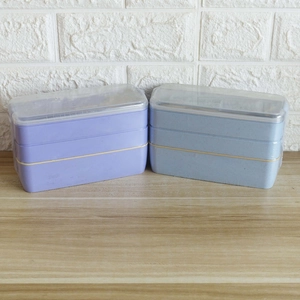 Three-layer wheat straw lunch boxes in purple and blue colors on a wooden table