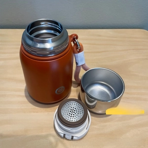 Detailed view of the orange thermos with 304 stainless steel lid and tea filter mesh