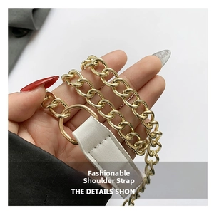 Detail of gold metal chain strap and white leather connector with fine white stitching