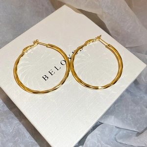 Detail view of 14k gold plated twisted hoop earrings on a white gift box with Beloved text