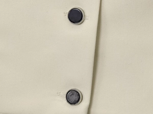 Detail von beigem Twill-Stoff und schwarz-silbernem Knopf an der ärmellosen Weste