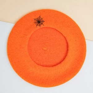 Top view of an orange wool beret featuring a detailed black spider web embroidery design