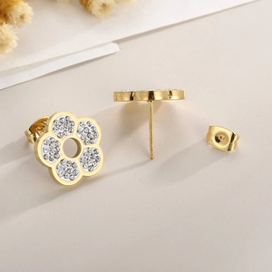Close-up of golden flower stud earrings with clear sparkling crystals on textured paper