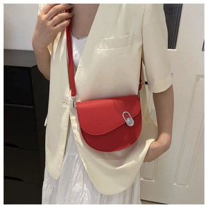 Close-up of red saddle bag with silver buckle worn by a model in a studio setting