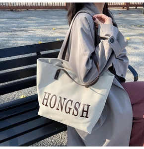 Detail of canvas tote bag showing dark brown leather shoulder straps and letter print