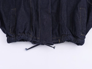 Détail de l'ourlet d'une veste en jean bleu foncé avec cordon de serrage et surpiqûres