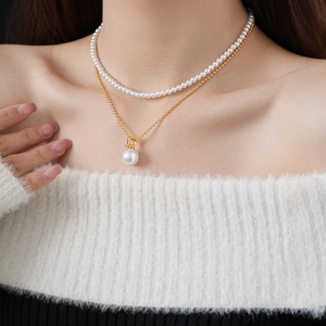 Detail of layered gold-plated necklace with white pearls and a gold letter D pendant
