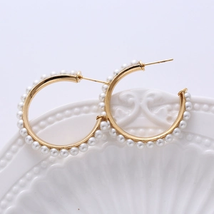Close-up of gold C-shaped twisted earrings with pearls on white ceramic plate