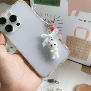 Detailed view of white flocked cat charm with pink bow hanging from clear phone case
