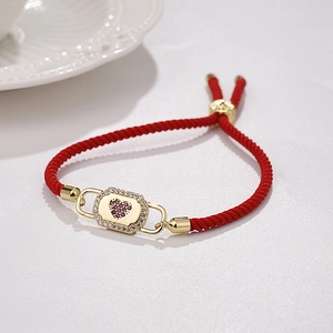 Detail of red woven bracelet with gold-plated heart lock pendant and purple zircons