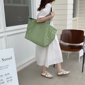Outdoor street shot of a large green and white plaid tote bag on a model in white dress