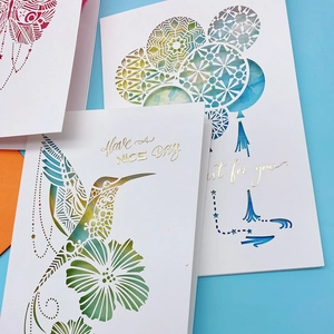 Detail of laser-cut 3D greeting cards with colorful watercolor backing and gold text