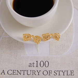 Gros plan de boucles d'oreilles nœud dorées avec texture de lave sur une tasse blanche