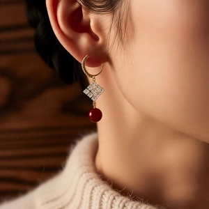 Gros plan de boucles d'oreilles dorées 18 carats avec losange diamanté et perle rouge