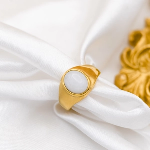 Detail of vintage 18k gold plated ring with oval white gemstone on white silk fabric
