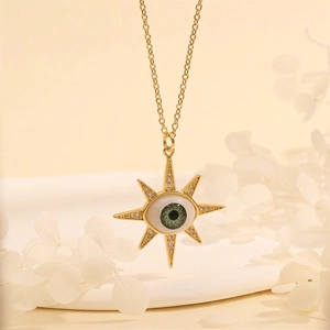 Detail view of 18K gold starburst evil eye pendant with green stone and crystals