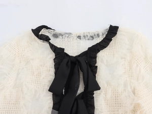 Détail du haut en dentelle beige avec encolure à volants noirs et nœud élégant