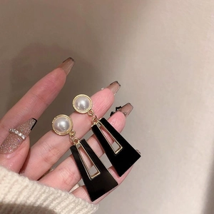 Detail view of long gold drop earrings with white pearls and black geometric pendants
