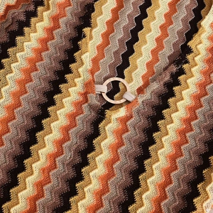 Detail of chevron knit fabric with brown tones and a decorative gold metal ring buckle