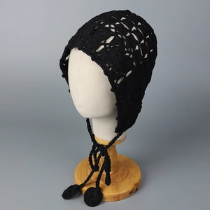 Détail du bonnet au crochet noir avec motifs floraux évidés et longs glands décoratifs