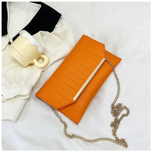 Detail of an orange faux leather clutch bag with horizontal texture and gold chain strap