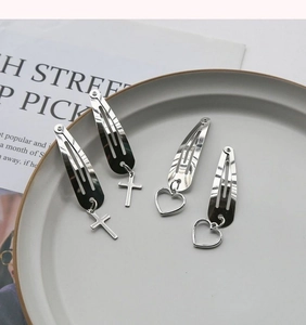 Silver metal BB hair clips featuring cross and heart pendants on a white ceramic plate