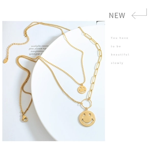 Detalle de collares de acero de titanio dorado con colgantes de sonrisa y dijes Good Luck