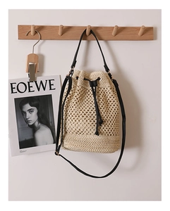 Detail of straw bucket bag with black leather strap hanging on a wooden hook