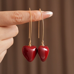Close-up of elegant red heart-shaped pendant earrings with gold hooks held by hand
